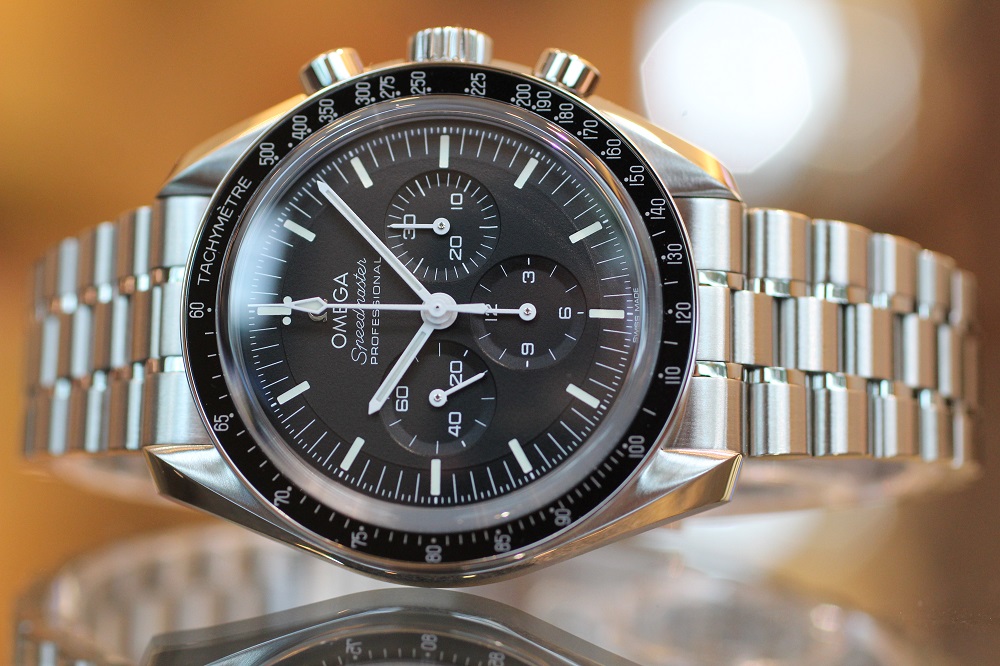 オメガ_スピードマスター ムーンウォッチ プロフェッショナル 42mm_310.30.42.50.01.002　針 スピードマスター ムーンウォッチの顔であるブラックの文字盤には、視認性を考慮した様々な工夫が凝らされています。その一つが、ホワイトの針とインデックスのコントラストです。 時針と分針には、視認性に優れたペンシル型の針を採用。クロノグラフ秒針には、一目で判別できるようセンタークロノグラフ針を採用し、スモールセコンド針には、リーフ型を採用しています。それぞれの針の形状を変えることで、瞬時に針の種類を判別することを可能にし、実用性を高めています。 文字盤色 文字盤の黒は、光沢を抑えたマットなブラックを採用。これは、強い光の下でも反射を抑え、時刻を読み取りやすくするための工夫です。また、ホワイトのインデックスや針とのコントラストが美しく、洗練された印象を与えます。 タキメーターベゼル ベゼルには、ブラックアルミニウム製のタキメーターベゼルを搭載しています。タキメーターとは、一定距離を走行した際の平均速度を計測するための機能です。例えば、1kmの距離を走行した際に、クロノグラフ秒針がベゼル上のどの数字を指しているかによって、平均速度を算出することができます。 このタキメーターベゼルは、スピードマスター ムーンウォッチにスポーティな印象を与えると同時に、その歴史を感じさせる重要なディテールとなっています。